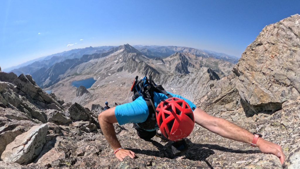 Hiker climbing the final ridge section on 14er Capitol Peak above an alpine lake in Colorado.