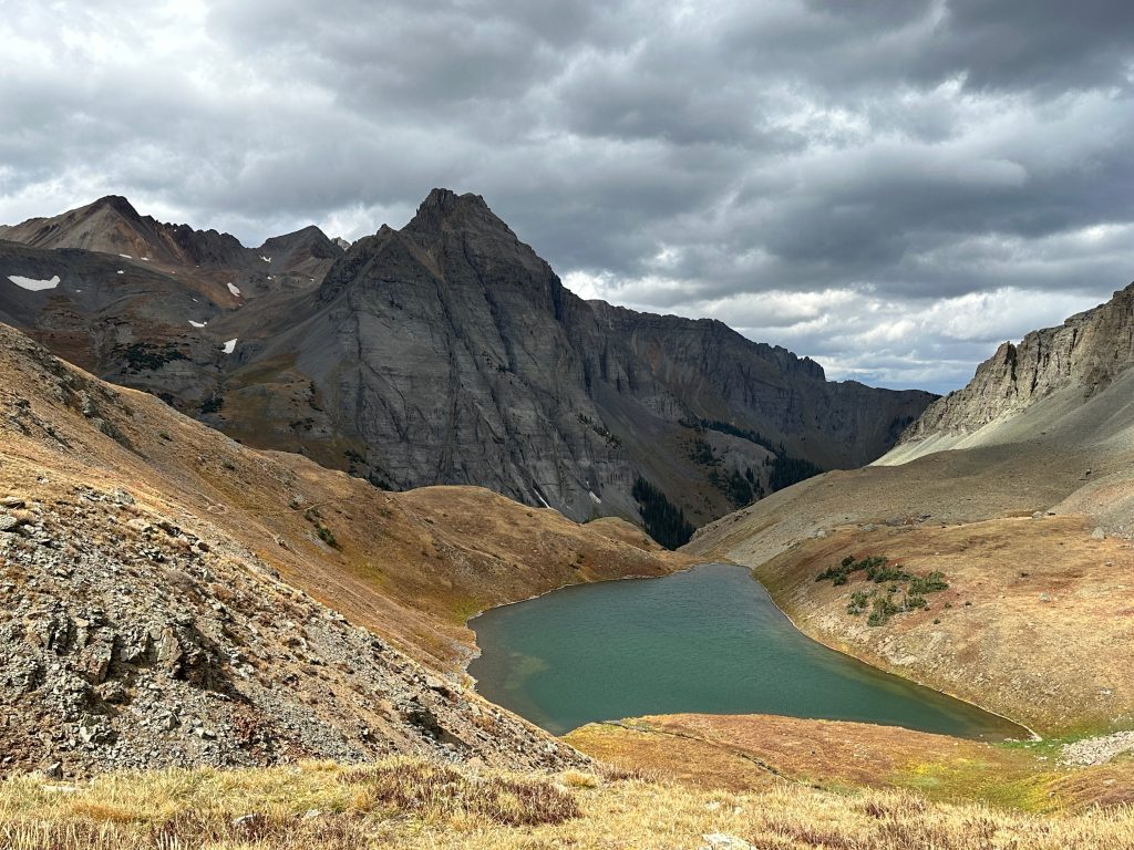 Upper Blue Lake nestled beneath dramatic mountain cliffs and storm clouds in the Blue Lakes Basin of Colorado.