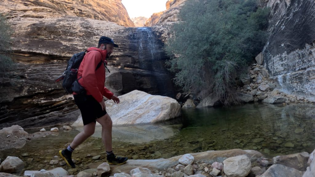 Hiker crossing a shallow pool beneath a small waterfall in Red Rock Canyon, Nevada.