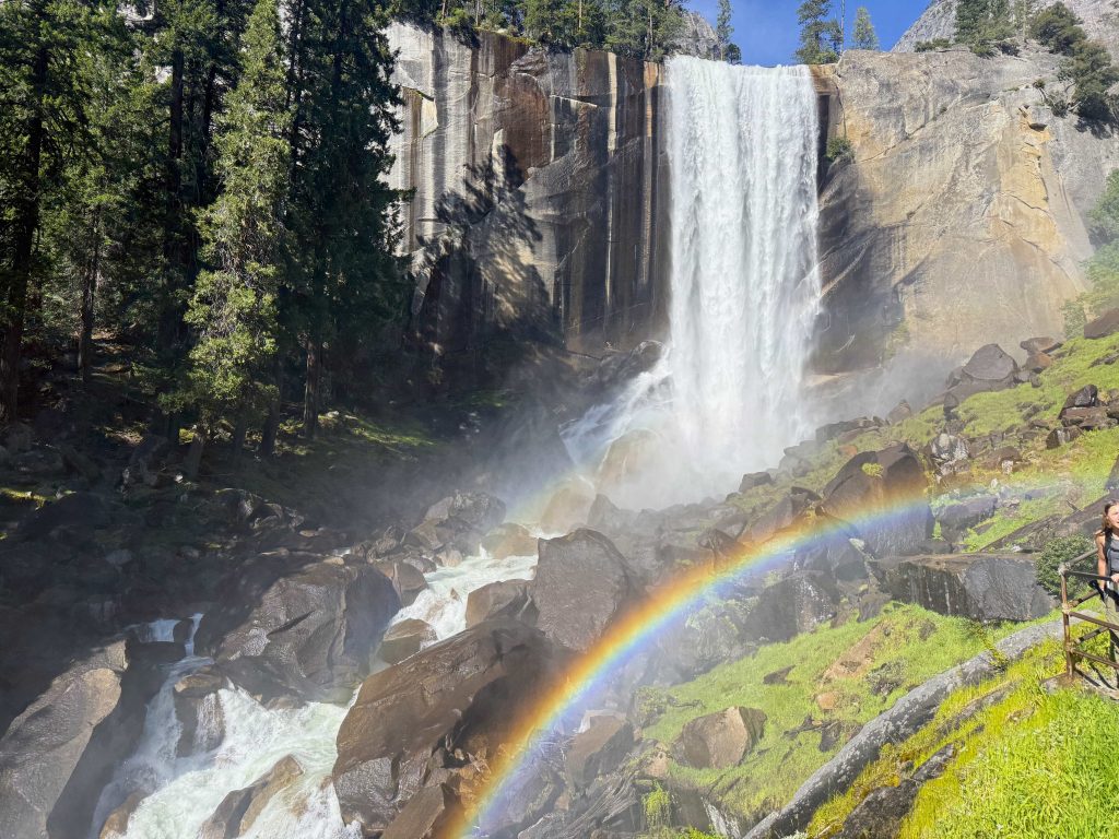 Rainbow forming in the mist at the base of Vernal Falls in Yosemite National Park on the Mist Trail with rushing water and granite cliffs.