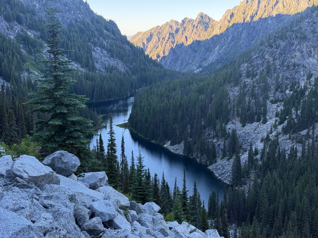 View of Nada Lake surrounded by evergreen forest and rugged granite mountains along the Enchantments Traverse in Washington's Alpine Lakes Wilderness.