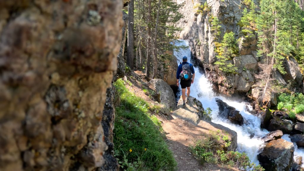 Hiker standing beside a waterfall on Cascade Creek along the trail to Crater Lake in Colorado.
