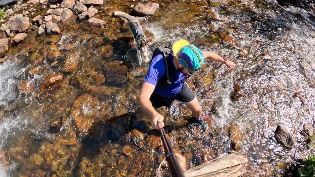Hiker and dog crossing a creek on the Gibraltar Lakes hike in Indian Peaks Wilderness.