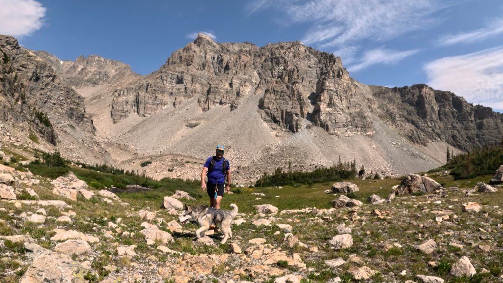 Hiker and dog below rugged peaks near Gibraltar Lakes in Colorado's Indian Peaks Wilderness.