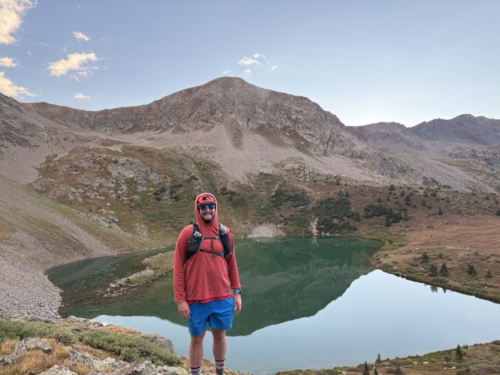 Hiker standing above Lake Ann on the Lake Ann Trail in Colorado with a turquoise alpine lake and rugged mountain peaks in the background