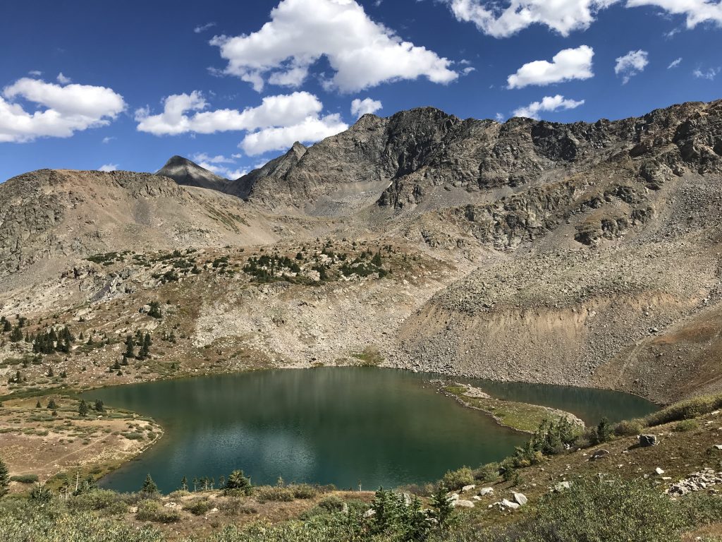 Panoramic view of Lake Ann surrounded by rocky mountain peaks and alpine tundra on the Lake Ann Trail in Colorado.