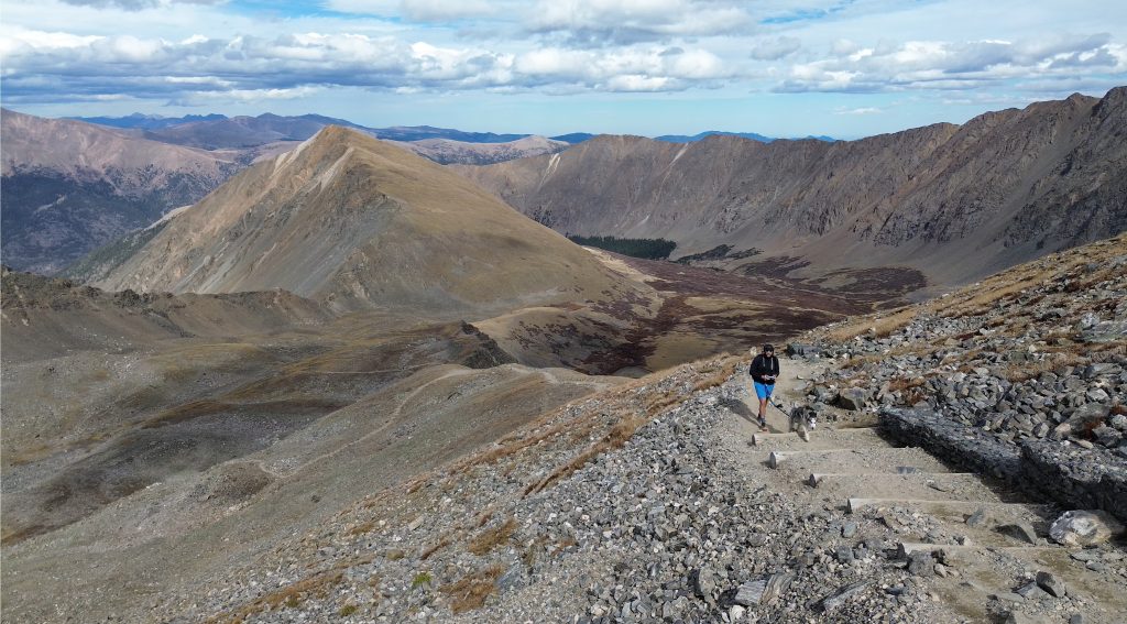 Hiker on the Grays Peak trail above treeline with surrounding mountain views.