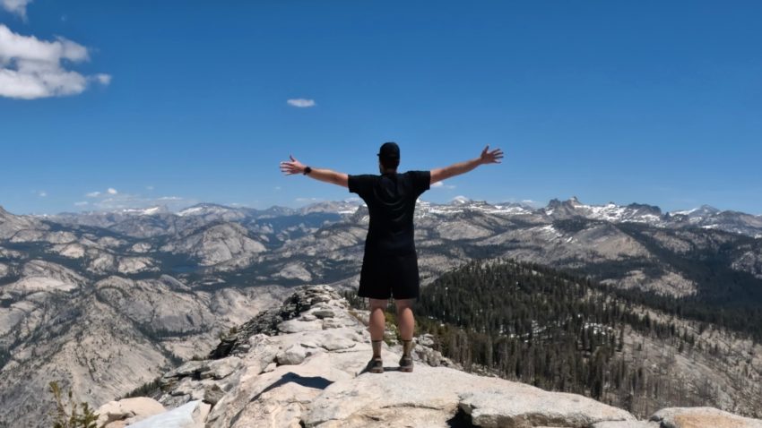 Hiker standing on the exposed summit ridge of Clouds Rest overlooking the Sierra Nevada mountain range.