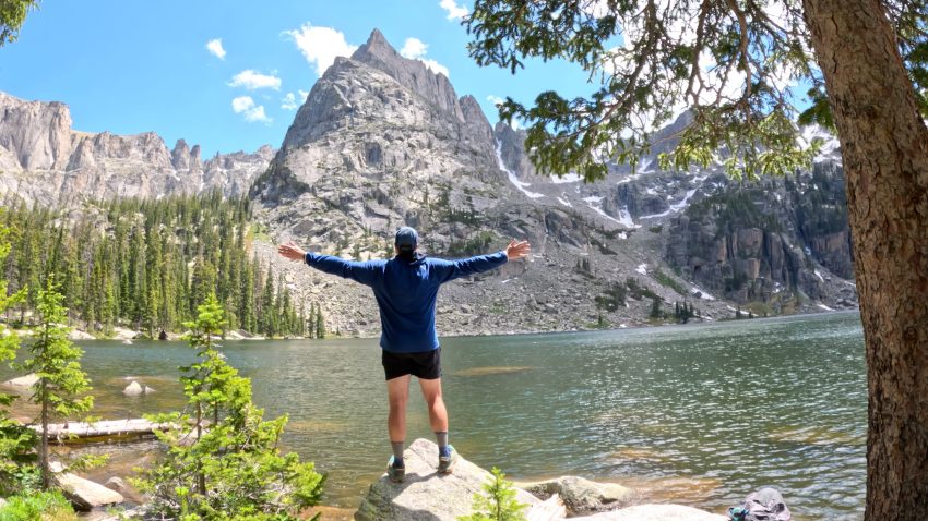 Hiker standing on a rock overlooking Crater Lake with Lone Eagle Peak towering above in the Indian Peaks Wilderness of Colorado.