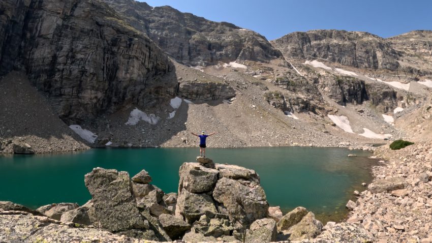 Gibraltar Lakes in Colorado's Indian Peaks Wilderness with a hiker standing above the turquoise alpine lake near Saint Vrain Glacier.